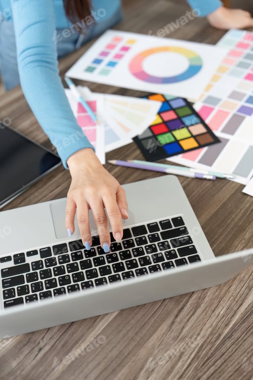 Preview: A designer types on a laptop while surrounded by colorful design materials and palettes.