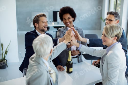 Preview: Successful business team gathering hands in unity while celebrating in the office.