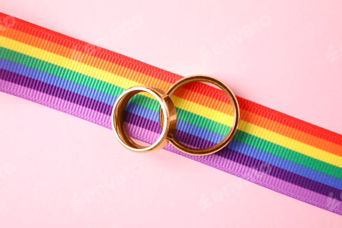 Preview: Wedding rings and rainbow ribbon on color background, top view. Gay symbol