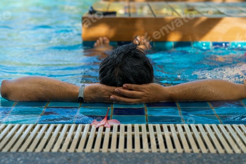 Preview: Back view of a tanned colour man relaxing in the swimming pool. Summer vacation