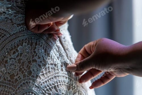 Preview: Closeup selective focus shot of a woman helping the bride zip her white dress