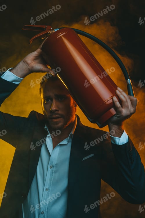 Preview: frightened caucasian man in suit holding fire extinguisher
