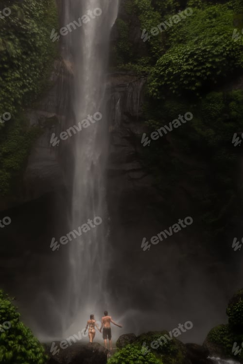 Preview: Young couple enjoying the freshness of nature under a waterfall in the tropics. The young pair