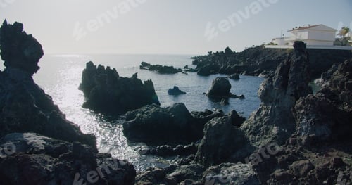 Preview: Wild beach with black volcanic lava stones on a sunny day.