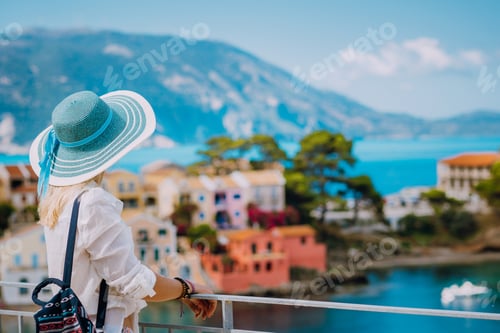 Preview: Tourist blond women with sun hat in cute colorful small Assos village. Kefalonia, Greece