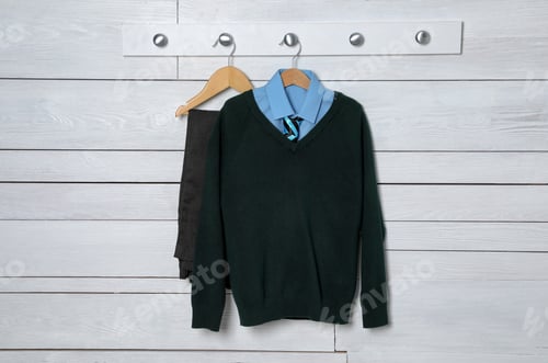 Preview: Shirt, jumper and pants hanging on white wooden wall. School uniform