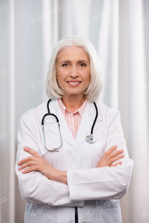 Preview: portrait of senior doctor with stethoscope and arms crossed looking at camera