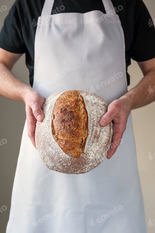 Preview: Close-up at bakers hands holding a loaf of bread in front of him.