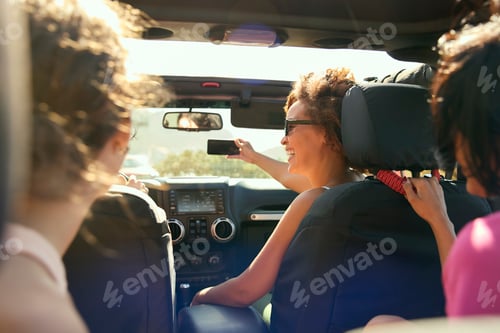 Preview: Laughing Female Friends Having Fun Posing For Selfie In Open Top Car On Road Trip