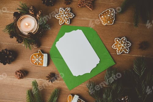 Preview: Christmas cookies and pine branches surround a green envelope with white card. Candle glows.