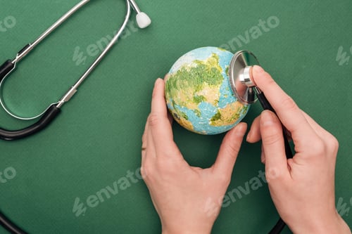 Preview: partial view of woman holding toy earth and stethoscope on green background