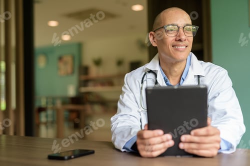 Preview: Doctor Sitting Indoors in Clinic or Hospital Area Library with Stethoscope using Tablet Computer
