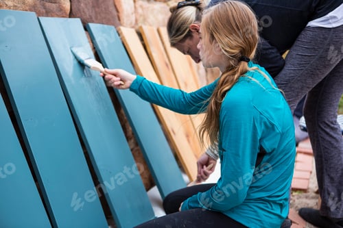 Preview: Teenage girl and her mother painting wooden shelves blue on a terrace