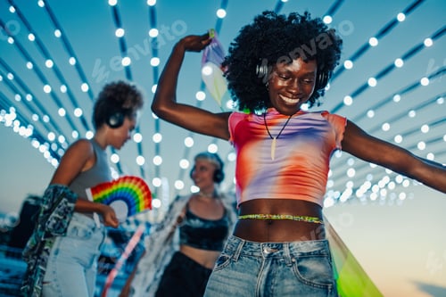 Preview: Young woman dancing with friends at music festival under string lights