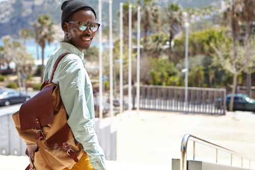 Preview: Cheerful excited young African American tourist with backpack walking along deserted streets of Euro