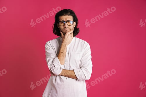 Preview: White puzzled man in eyeglasses holding his chin and looking at camera