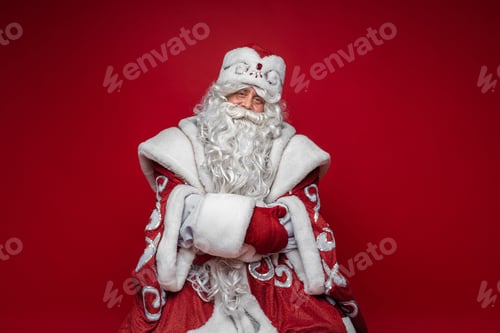 Preview: old caucasian father frost in long warm coat, red mittens and a hat looks to the camera