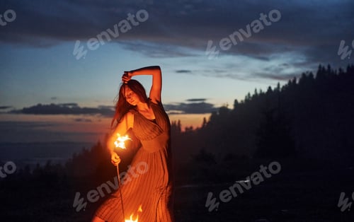 Preview: Fire show by woman in dress in night Carphatian mountains. Beautiful landscape