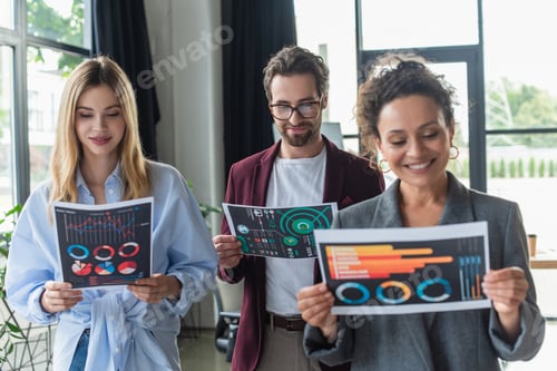 Preview: Businessman in eyeglasses looking at paper near multiethnic colleagues in office