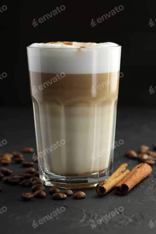 Preview: Tasty latte macchiato in glass, coffee beans and cinnamon on black table, closeup
