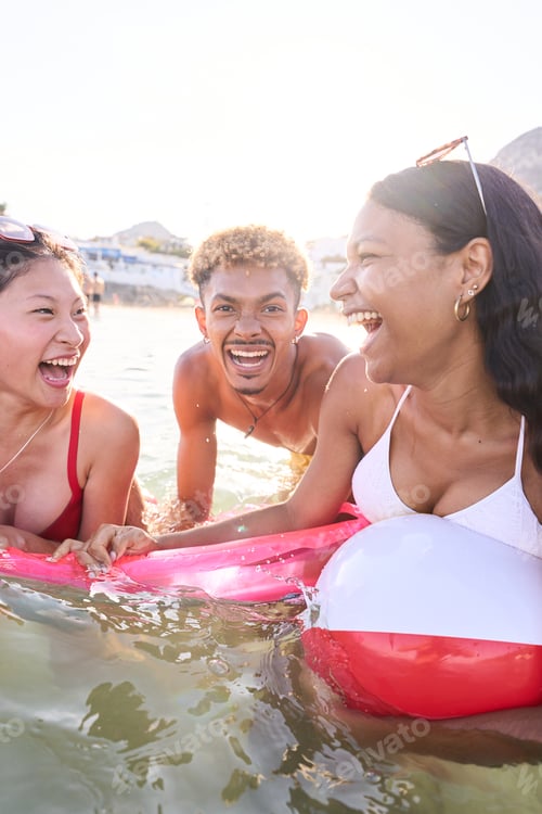 Preview: Three multiracial young people in swimwear laughing looking each other enjoying inside the sea.