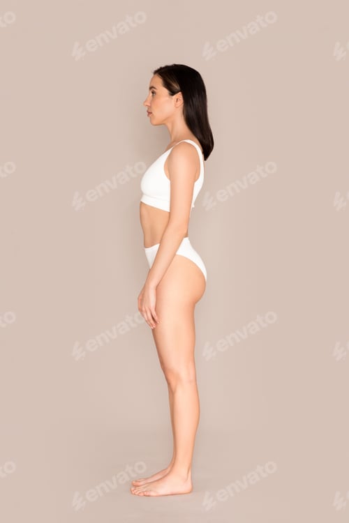 Preview: Young well-fit woman in underwear posing on beige, side view
