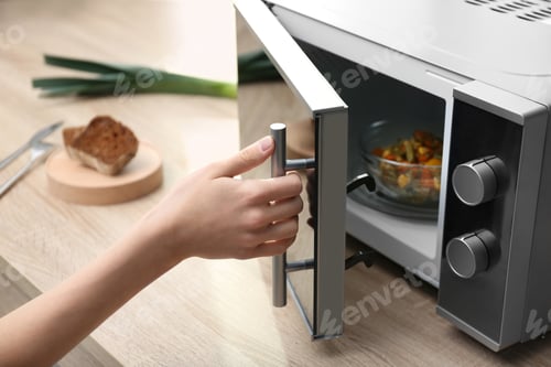 Preview: Young woman using microwave oven on table in kitchen