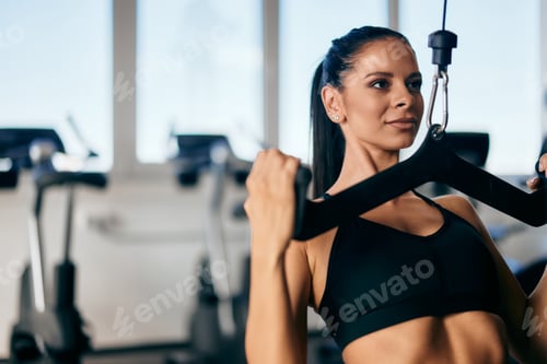 Preview: Gym girl doing an exercise for her back, a lat pull down, at the modern gym.