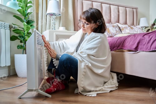 Preview: Woman warming herself at home near an electric heater