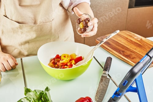 Preview: Teenager prepares salad from online learning, tossing olives and watching digital recipe