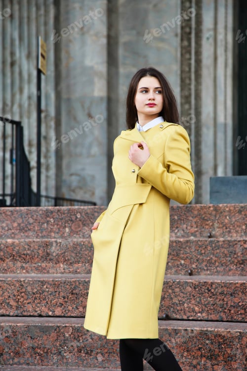 Preview: Young Woman Stands on City Steps Wearing a Stylish Yellow Autumn Coat