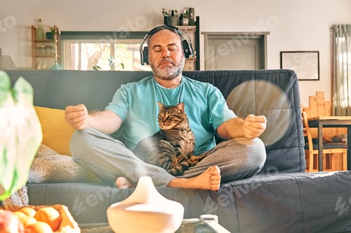 Preview: Mature middle-aged overweight man in wireless headphones meditation at home with his cat.