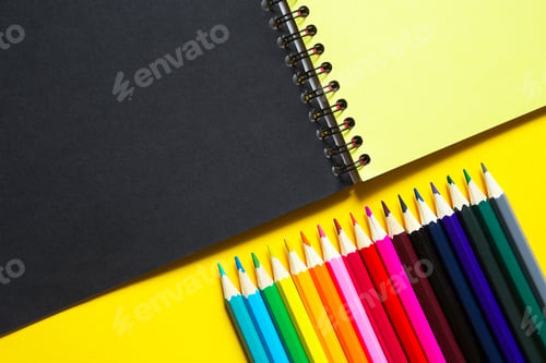 Preview: Rainbow palette of colored pencils with a spiral notebook on a yellow background