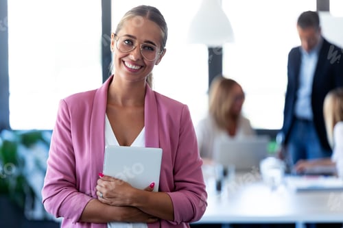 Preview: Smart young businesswoman looking at camera while holding her digital tablet on coworking place.