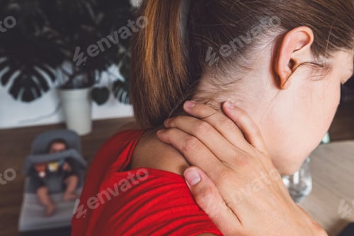 Preview: Woman massaging her neck with a baby in the background. Neck pain because of looking to to the lapto