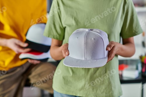 Preview: Cropped view of young african american designer holding snapback while standing near blurred