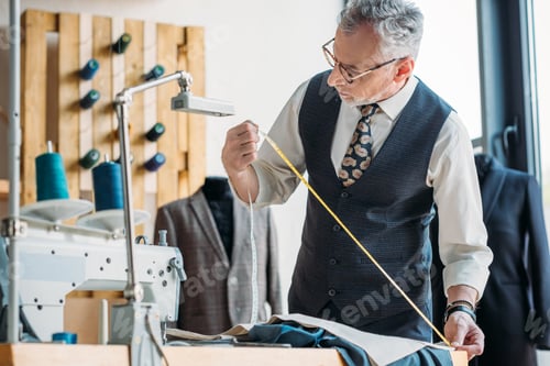 Preview: grey hair tailor measuring cloth with tape measure at sewing workshop