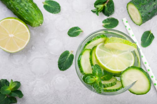 Preview: Refreshing water with cucumber, mint and lime on grey background top view. Summer drink