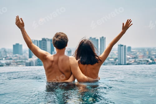Preview: Young happy couple in love with arms up having fun in swimming pool