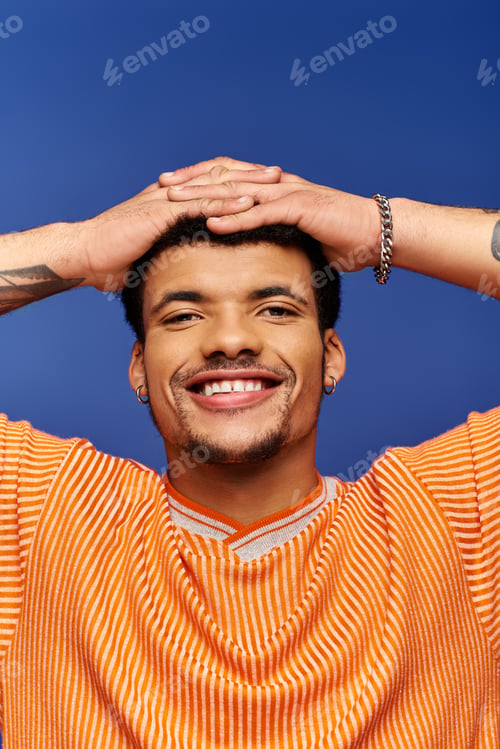 Preview: Charming man with a joyful smile poses playfully against a vibrant blue backdrop