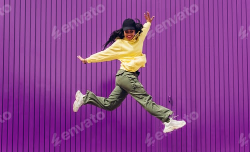 Preview: Jumping young woman in yellow dress on purple background. Dancer of hip hop and trap music