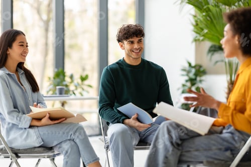 Vista previa: Happy multiracial students friends talking and discussing educational project together, sitting on