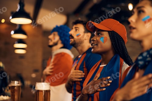 Preview: Group of fans singing national anthem while watching sports match in a pub.