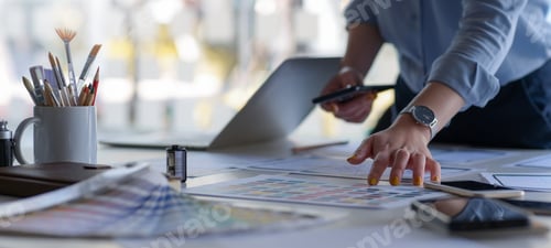 Preview: Graphic designer holds a smartphone with color charts and office equipment on work desk.