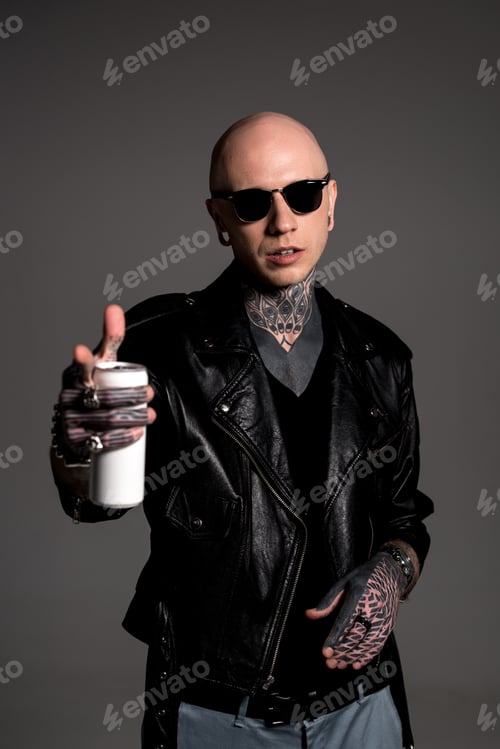 Preview: bald tattooed man in leather jacket and sunglasses holding soda can and pointing at camera isolated