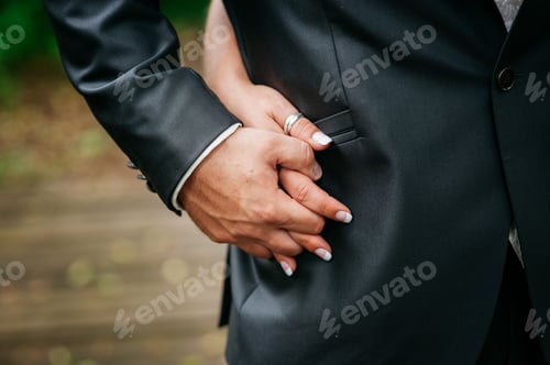 Preview: Closeup of the bridegroom holding firmly bride's hand and keeping in his costume