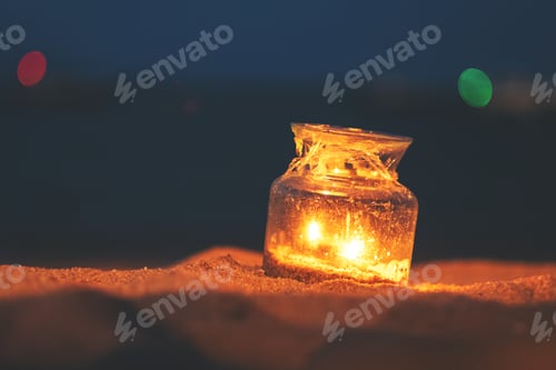 Preview: Closeup image of a glass bottle candles holders on the beach at night