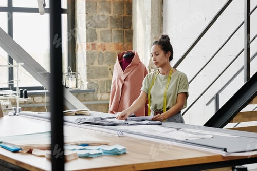 Preview: Young pretty designer of clothes in casualwear looking through new sketches