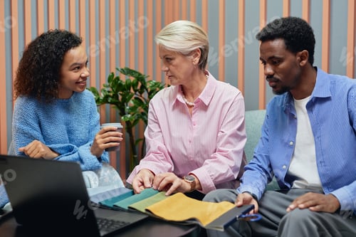 Preview: Senior Businesswoman Choosing Fabric on Color Samples with Diverse Team in Coworking Lounge