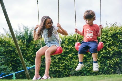 Preview: Two kids enjoying a sunny day on the swing set in a lush green park
